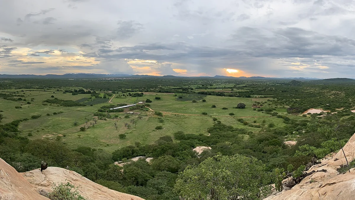 Paisagem rural do sertão ao entardecer, com vale cultivado e serras ao fundo
